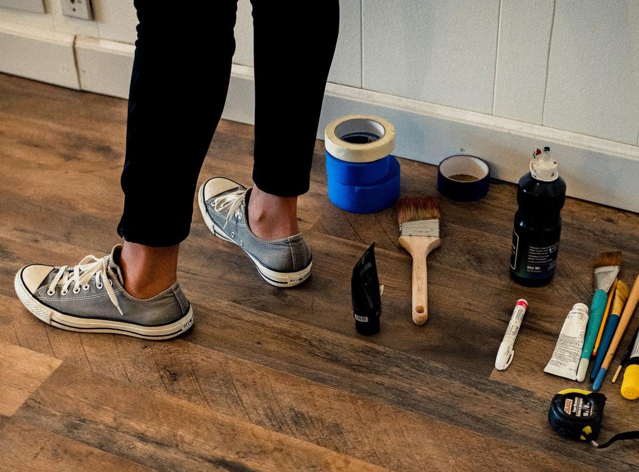 person in black pants and white and black nike sneakers standing on brown wooden floor